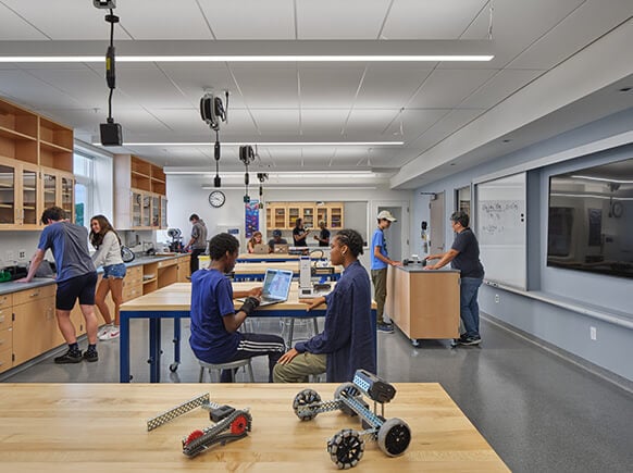Students engage in hands-on learning in a classroom with workstations, robotics kits, and technology displays. Tables promote collaboration and creativity.