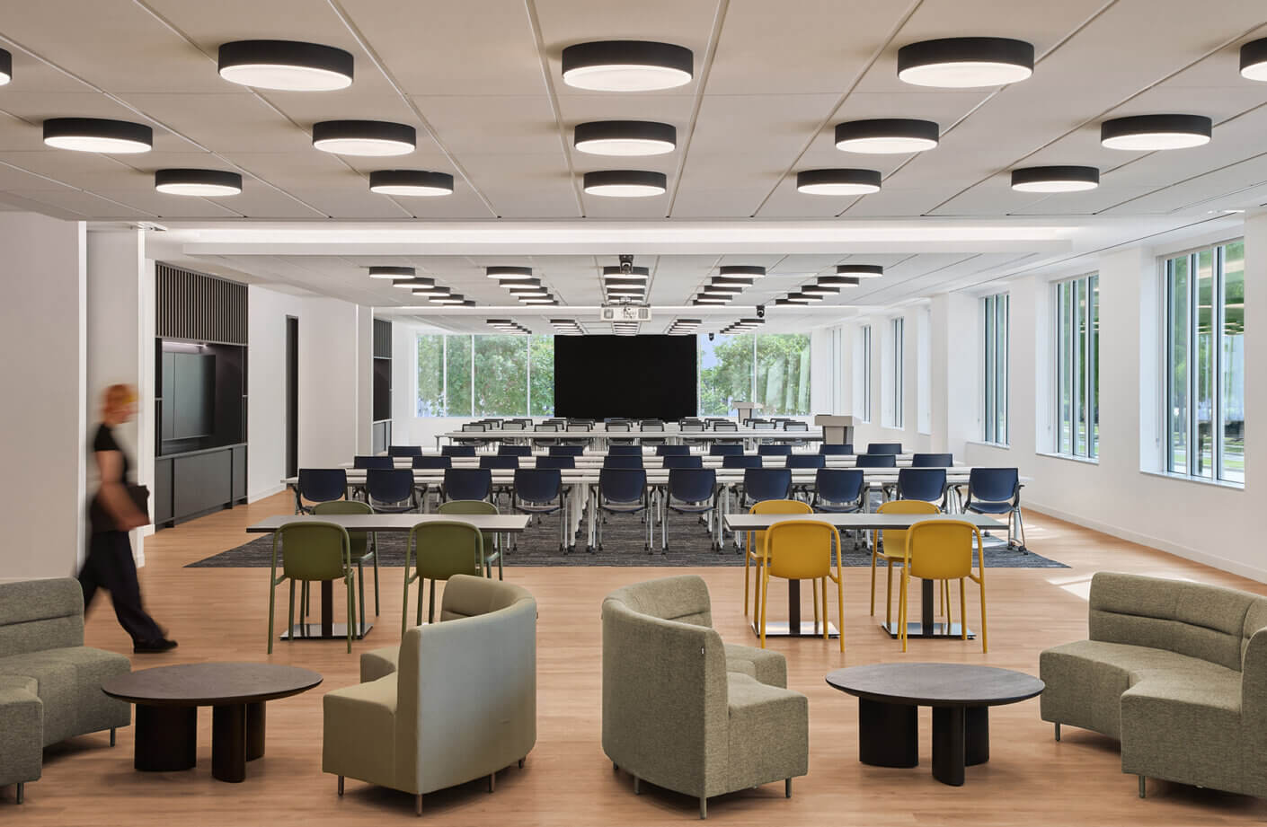 Interior view of a classroom with rows of chairs and tables, featuring light fixtures and seating areas for group work or meetings.