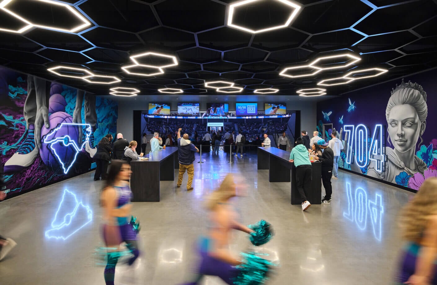 Interior view of a lively venue with a large mural, vibrant lighting, and people mingling at a bar area, exhibiting a sports atmosphere.