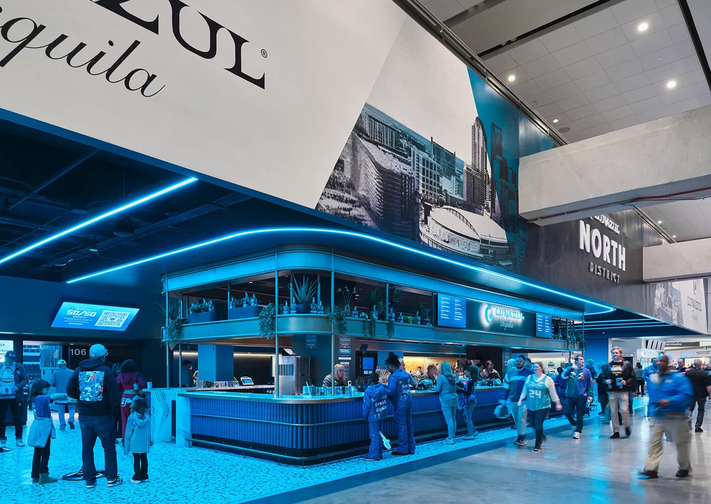 Bar area in a sports venue, featuring Azul and Lunazul branding, with people enjoying the space under blue lighting.
