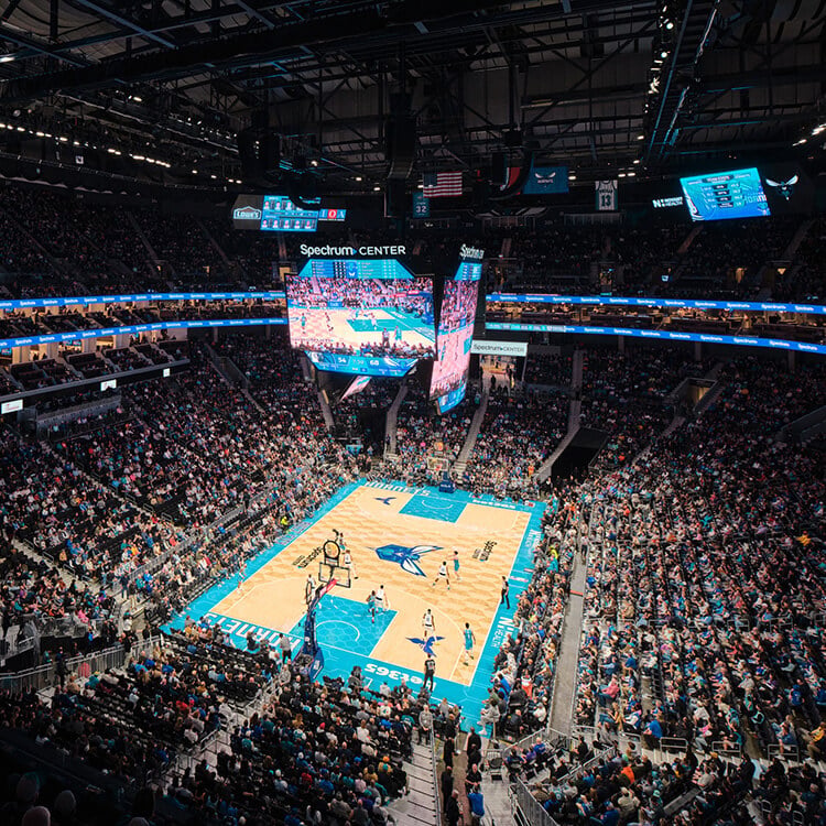 Basketball game in progress at Spectrum Center, with a packed crowd and large screens displaying the action on the court.