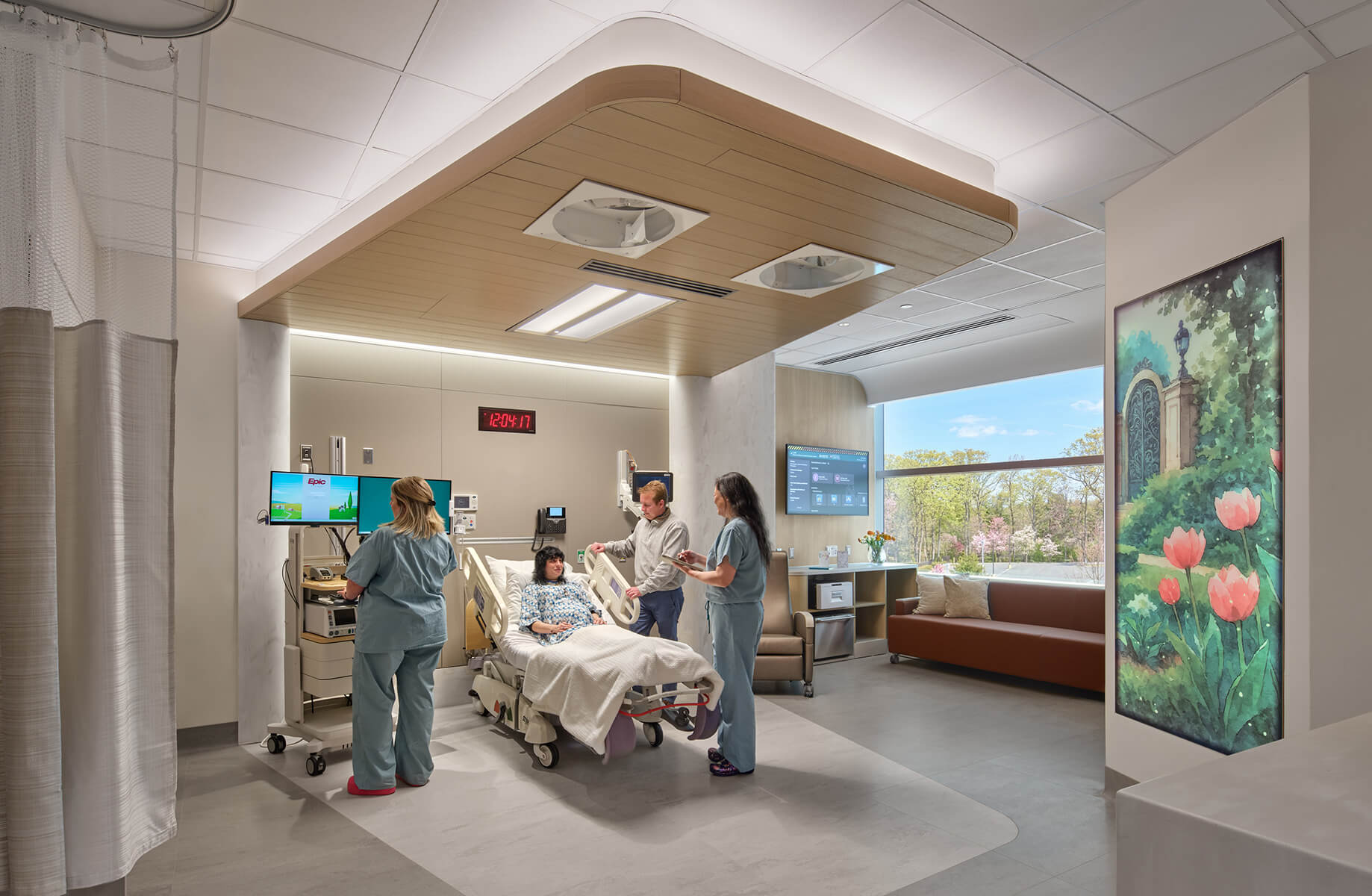 Healthcare professionals interact with a patient in a hospital room equipped with medical technology, natural light, and comfortable seating.
