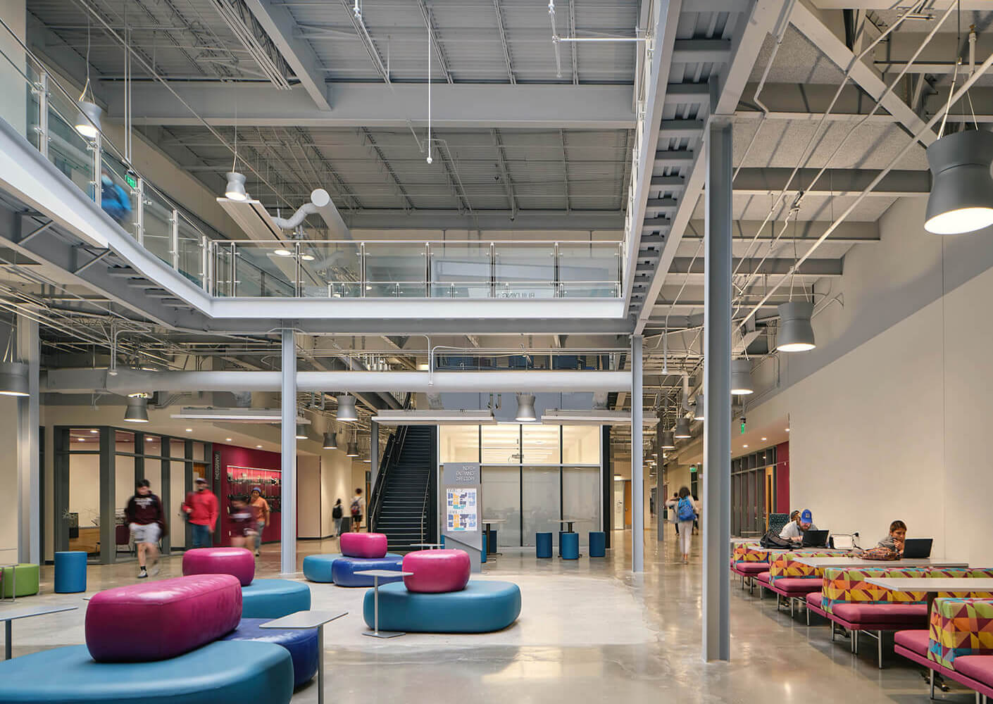 Interior view of a spacious building featuring colorful seating arrangements, open upper levels, and people engaging in various activities.