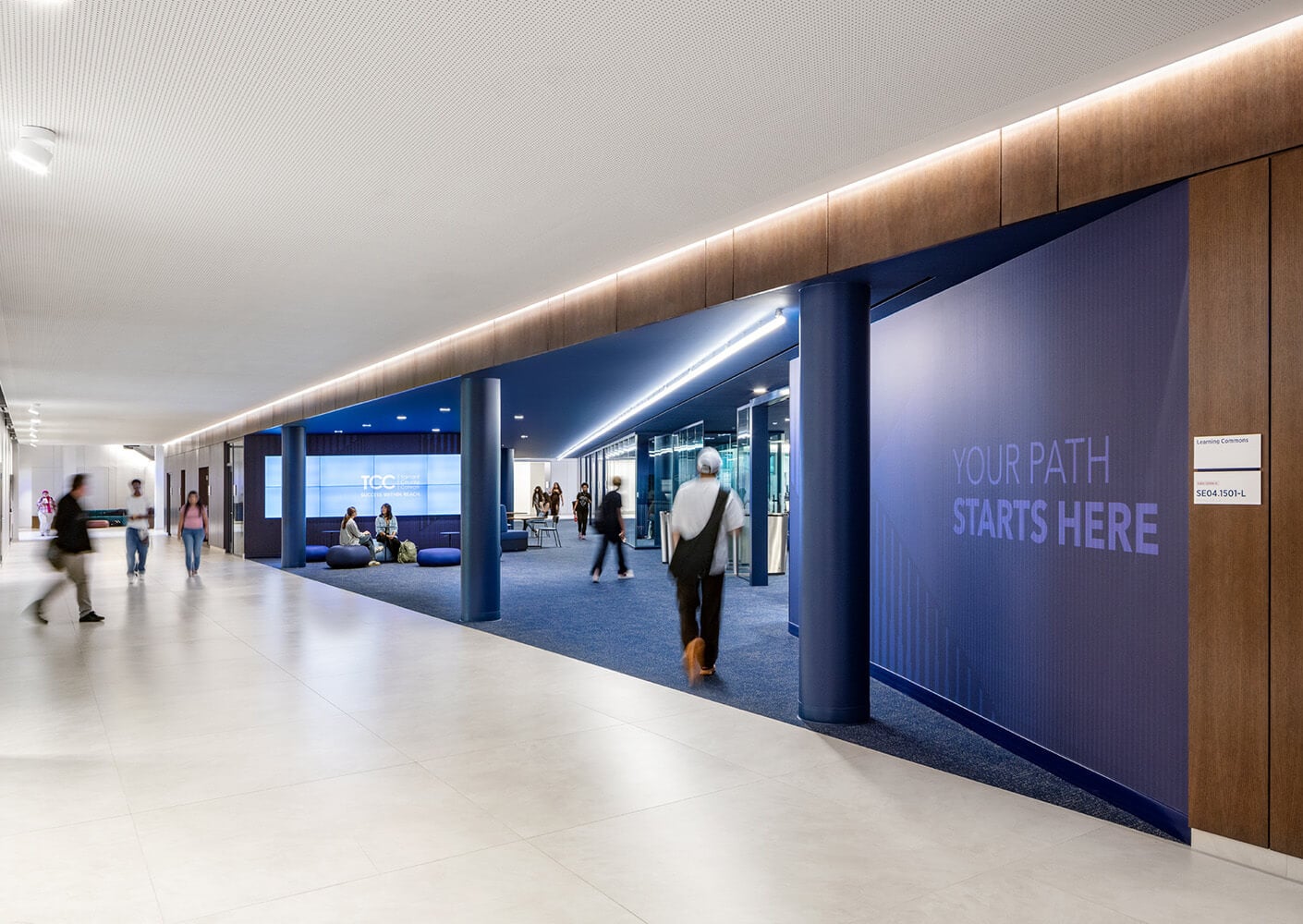 Interior view of a university corridor featuring seating areas, digital displays, and students interacting in a spacious layout.