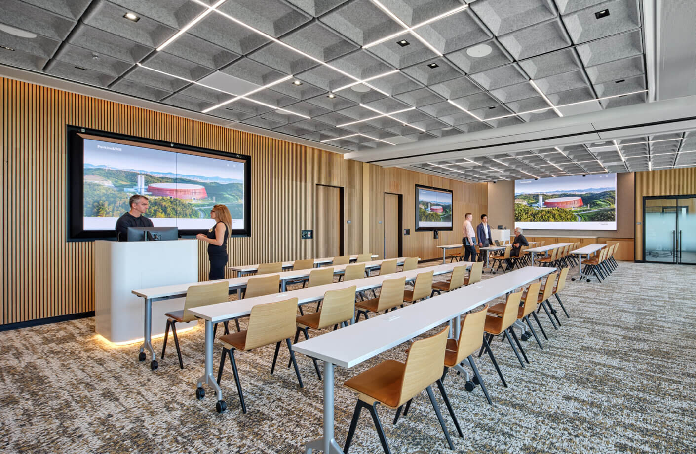 Conference room with arranged seating, large screens displaying presentations, and professionals engaging in conversation.