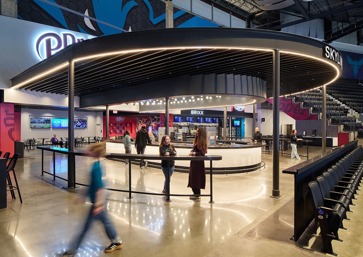 Interior view of a sports venue with a bar area named Brixx, featuring patrons and multiple screens, showcasing a vibrant atmosphere and seating options.